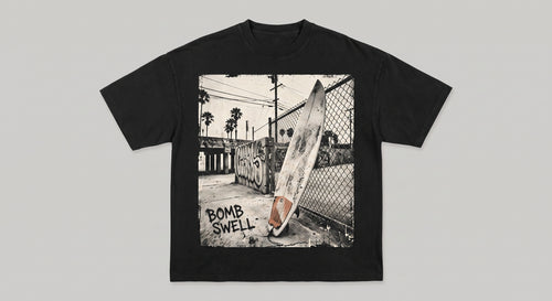 Camiseta oversize negra con estampado fotográfico de una tabla de surf apoyada en un callejón urbano